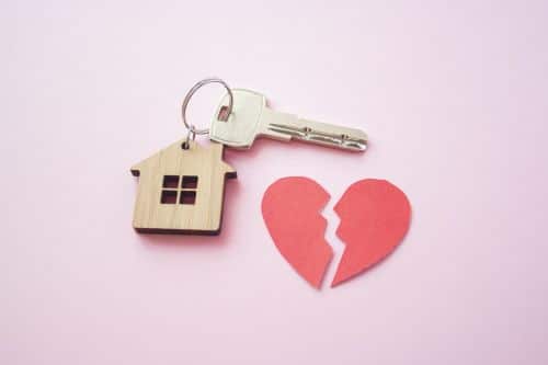 wooden house keychain with a broken heart on pink background - what happens to the house in a divorce concept