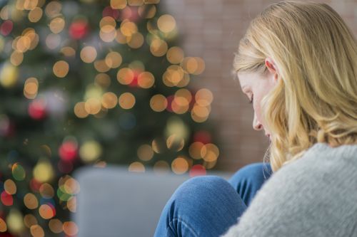 woman looking sad with a christmas tree in background