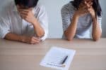stressed out couple sitting at a table with divorce settlement paperwork on it - diy divorce concept